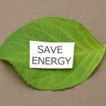 grünes Buchenblatt auf dem ein Zettel mit der Aufschrift "SAVE ENERGY" liegt.
