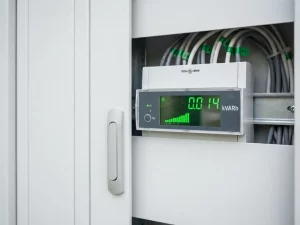 Digitaler Energiezähler mit grünen LED-Anzeigen für Blindleistung in weißem Schaltschrank bei Tageslicht.