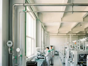 Industrielle Druckluftanlage mit Manometern und Metallarmaturen in einer hellen Produktionshalle mit natürlichem Tageslicht.