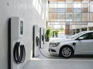 Weiße Elektroauto-Ladestationen in modernem Firmenparkhaus, silbernes Dienstfahrzeug wird geladen, grüne LED-Anzeigen leuchten.