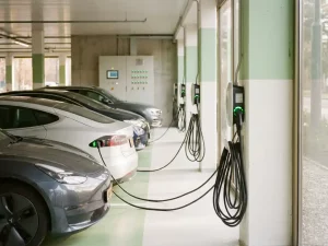 Elektrofahrzeuge in ordentlichen Reihen an modernen Ladestationen in einem hellen Firmenparkhaus mit grünen Kontrollleuchten.