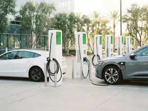 Zwei Elektroautos laden gleichzeitig an modernen Ladesäulen in einem hellen Firmenparkplatz mit grünen Akzenten.