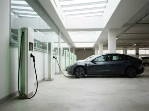 Reihe weißer EV-Ladestationen in hellem Parkhaus mit grüner Akzentbeleuchtung und angeschlossenem Elektroauto.