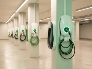 Weiße EV-Ladestationen mit grünen LED-Anzeigen in einer modernen, beleuchteten Tiefgarage mit geordnetem Kabelmanagement.